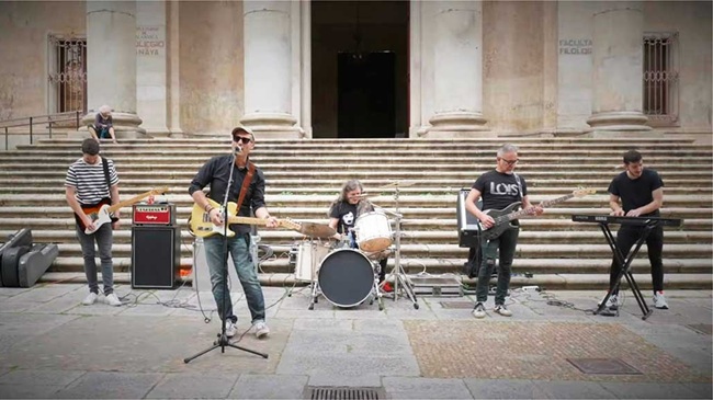 Juanjo Valle y su banda de pop-rock tocando en directo con guitarras, bajo, batería y teclado frente a las columnas de la Facultad de Filología en la Plaza de Anaya, Salamanca.