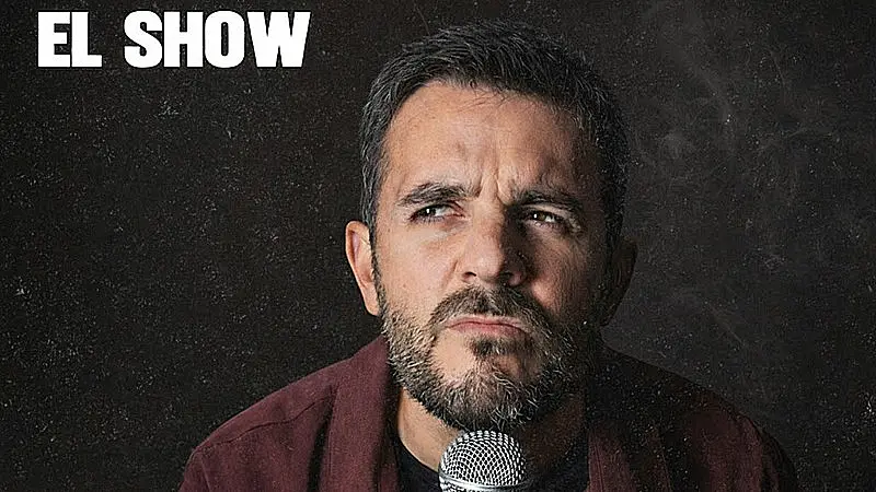 Primer plano del cómico Edén Serrano con expresión reflexiva frente a un micrófono, promocionando su espectáculo de humor.